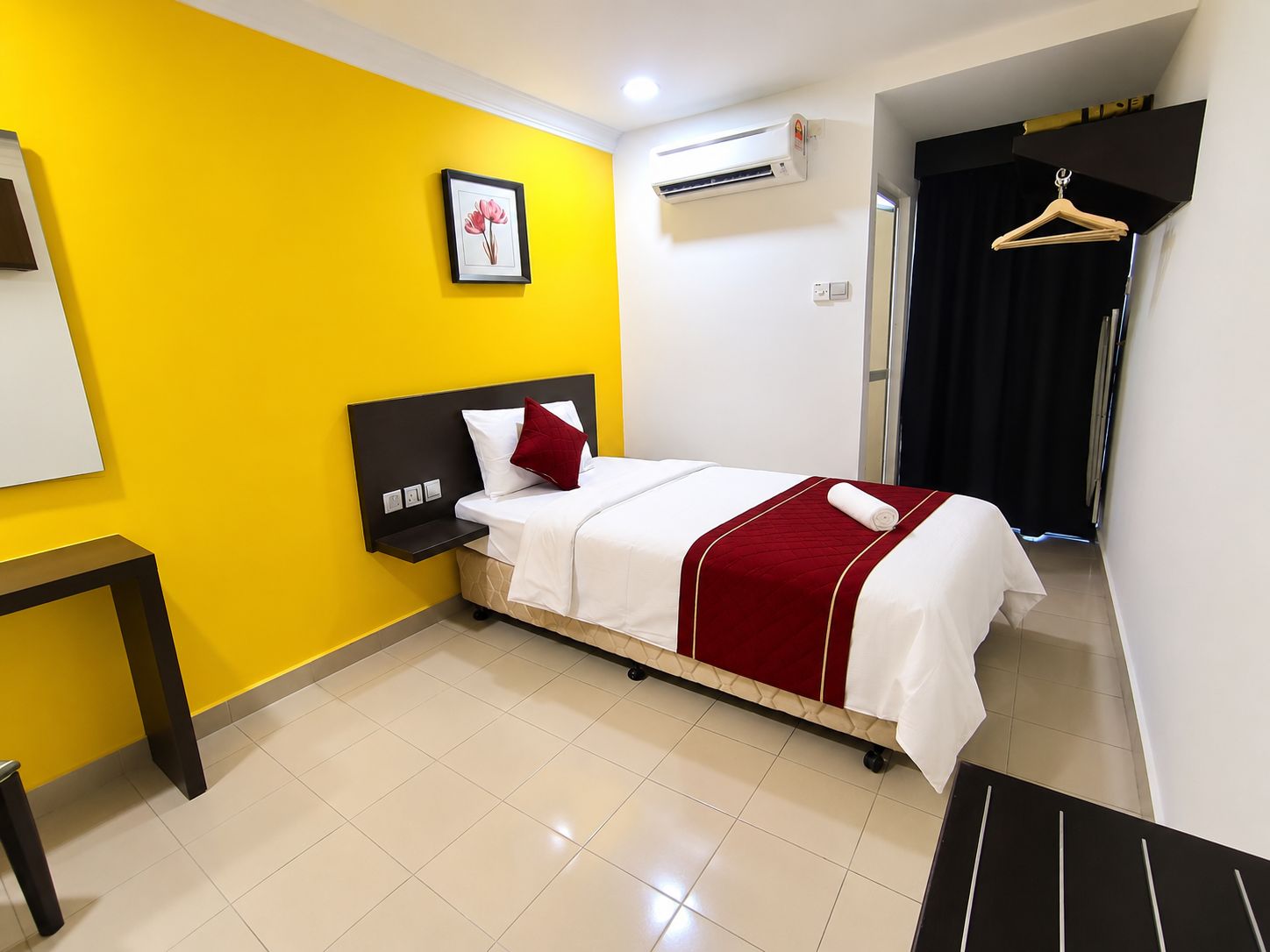 A hotel room with a bed, a bedside table, a hanging coat rack, and a picture on the wall.