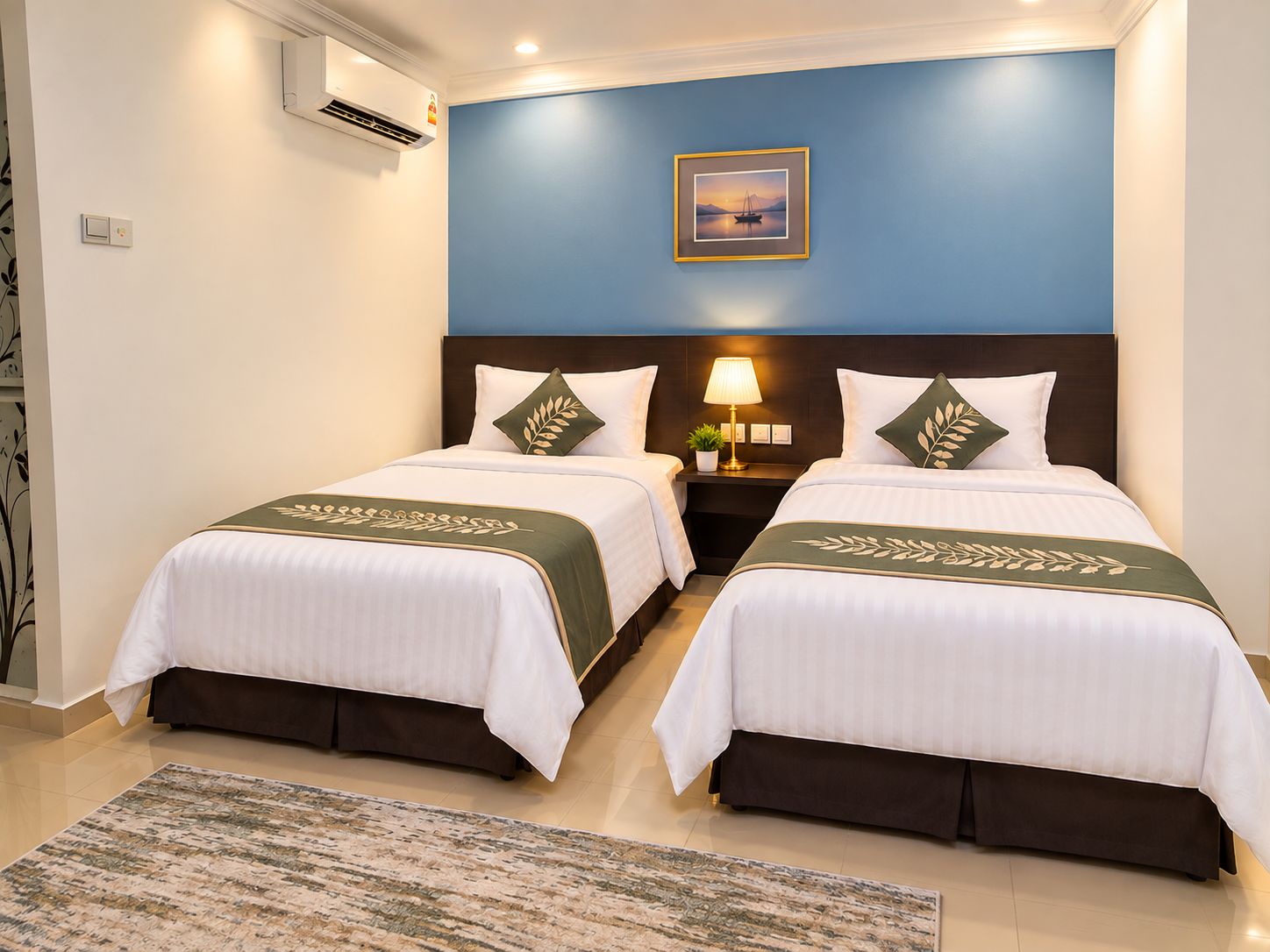 A hotel room with two beds, a nightstand with a lamp, a framed picture on the wall, and a patterned rug.