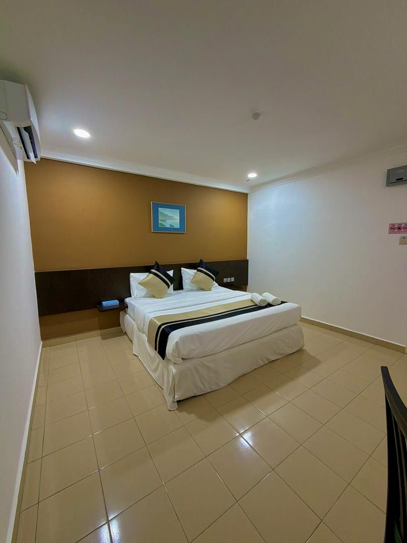 A hotel room with a bed, bedside table, and an air conditioning unit.