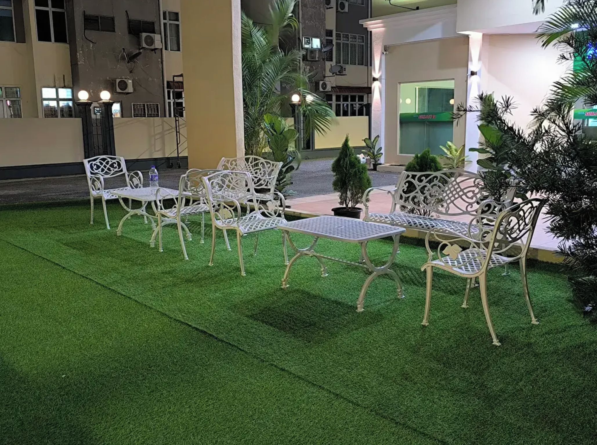 An outdoor seating area with white metal chairs and tables, surrounded by artificial green turf.