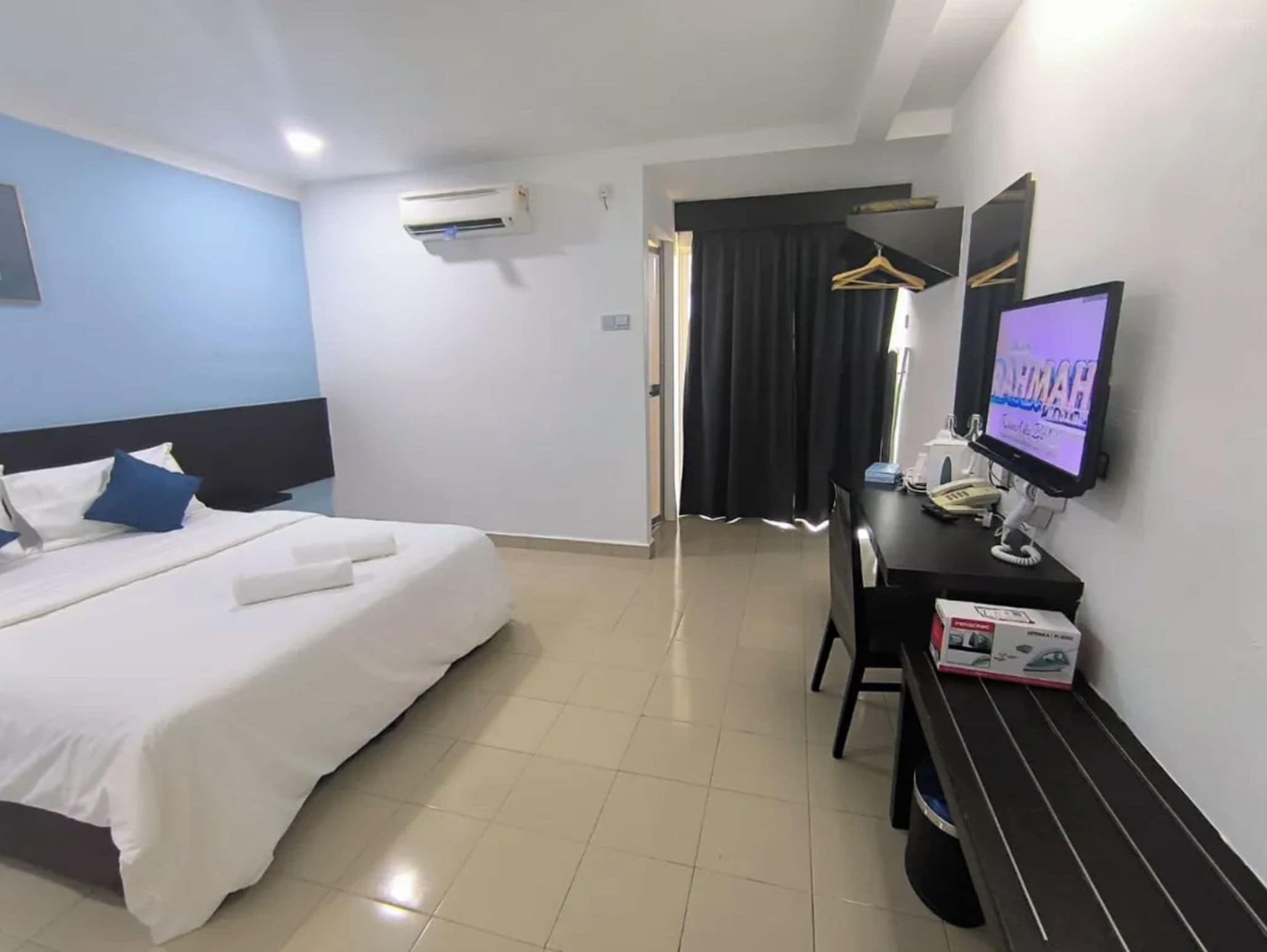 Quarto de hotel com cama, escrivaninha com computador, televisão e guarda-roupa.