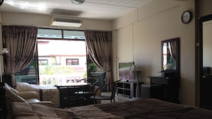 A hotel room with a large bed, a desk with a chair, a TV, and an air conditioning unit. - Artem's Guesthouse (Pattaya)