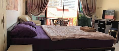 A bedroom with a bed, a chair, a table, and a TV.