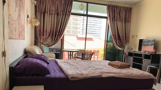 A bedroom with a bed, a chair, a table, and a TV. - Artem's Guesthouse (Pattaya)
