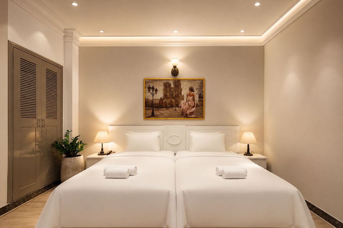 A double bed with two nightstands, a painting above, and a potted plant on the left.