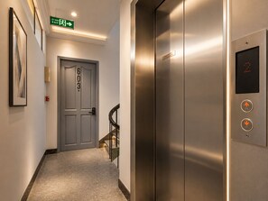 A hallway with an elevator, a door marked '603', and a green exit sign. - KAS Elegance Hotel (Ben Thanh Ward)