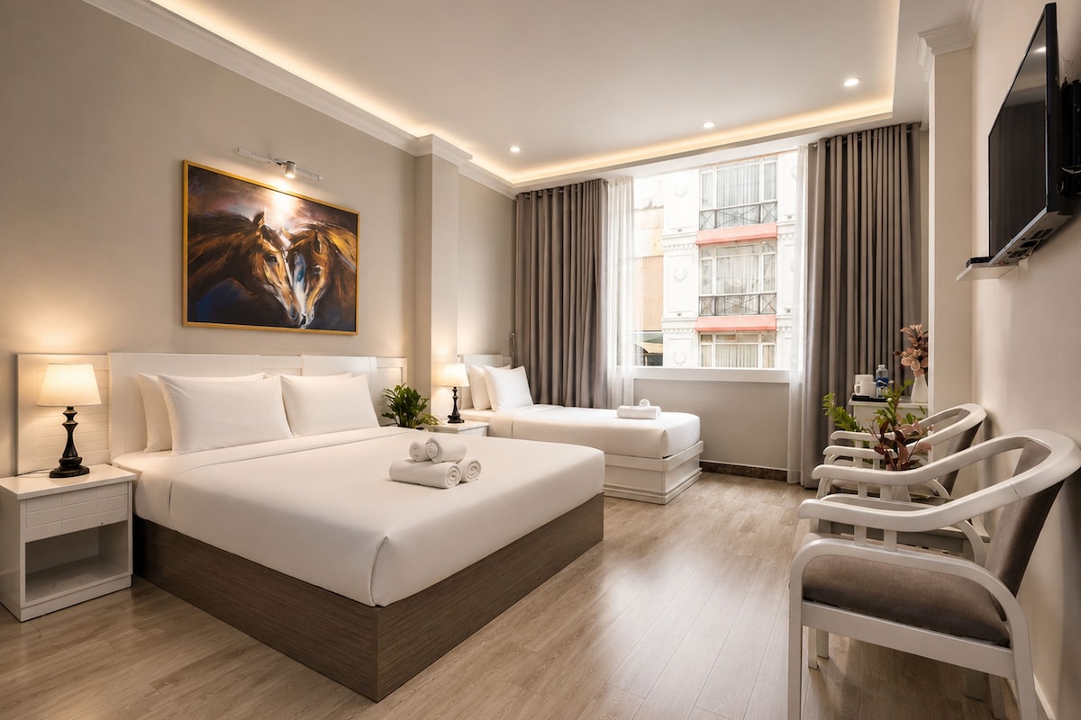A hotel room with a large bed, two bedside tables, a flat-screen TV, a window with curtains, and a painting on the wall.