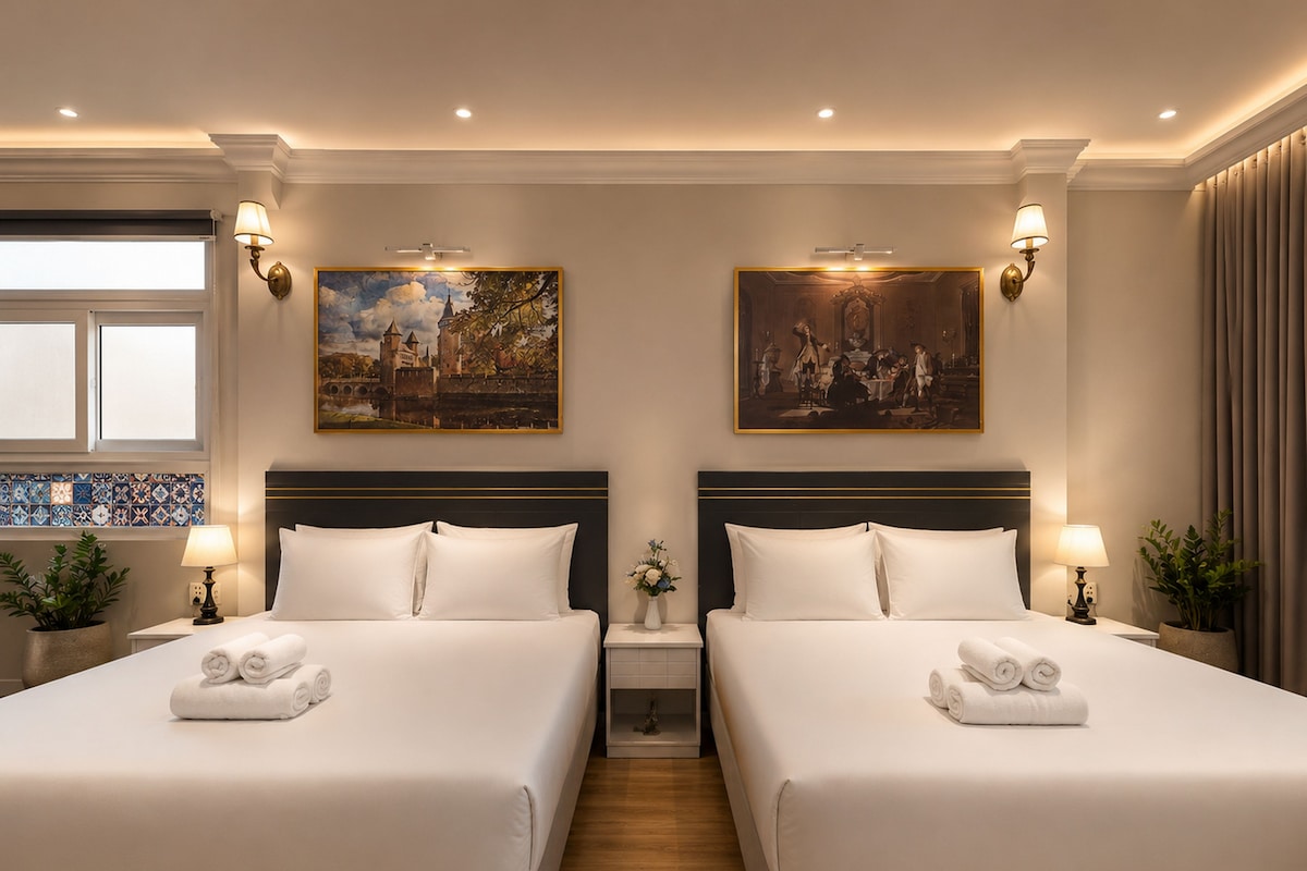 A hotel room with two beds, a painting above each bed, a window with blinds, and a plant on the nightstand.