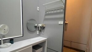 A bathroom with a white vanity, a mirror, a towel rack, and a shower area.