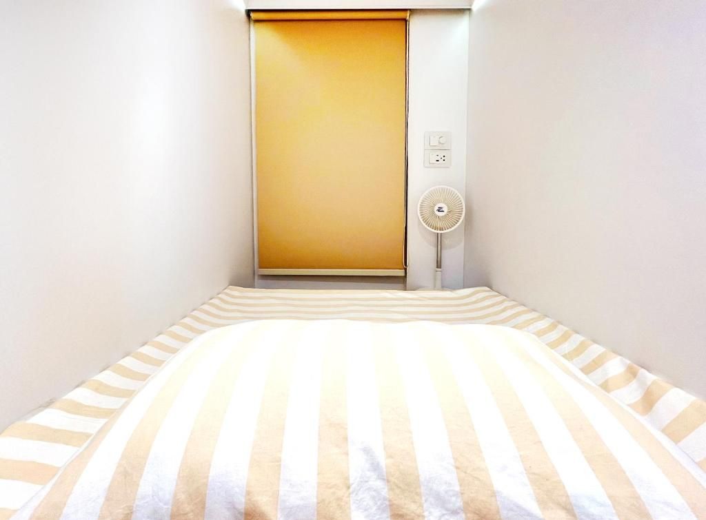 Une pièce avec un lit, une porte fermée et un ventilateur fixé au mur.