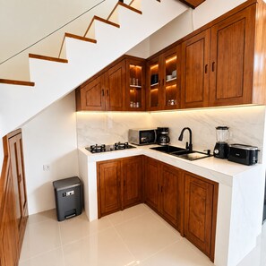 Een moderne keuken met houten kastjes, een marmeren aanrecht, een gasfornuis, een spoelbak, een koffiezetapparaat en een blender.