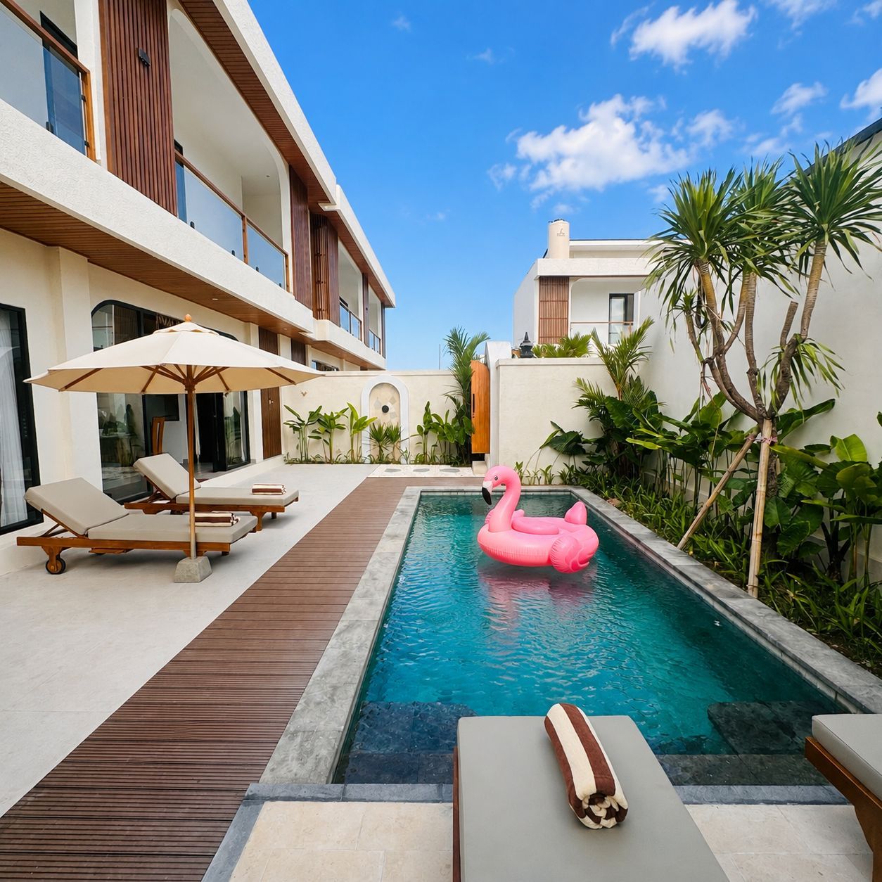 A pool area with lounge chairs and a pink flamingo float.