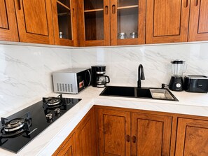 Een moderne keuken met houten kastjes, een ingebouwde magnetron, een koffiezetapparaat, een blender, een broodrooster en een gasfornuis.