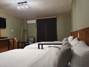 Ett hotellrum med en säng, ett skrivbord, en stol, en tv och ett fönster med gardiner.