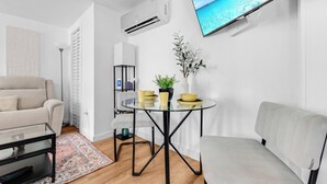 A modern living room with a sofa, a glass table with yellow bowls, a potted plant, and a mounted TV. - Chic 1BR Loft w/ Backyard near Pearl & Downtown (San Antonio)
