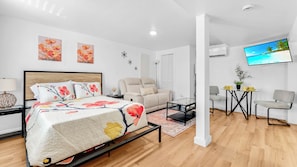 Quarto moderno com cama, sofá, televisão e uma mesinha com uma planta.