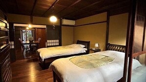 A traditional Japanese-style room with two beds, wooden flooring, and a sliding door leading to a dining area. - Shimoza-an (Kyoto)
