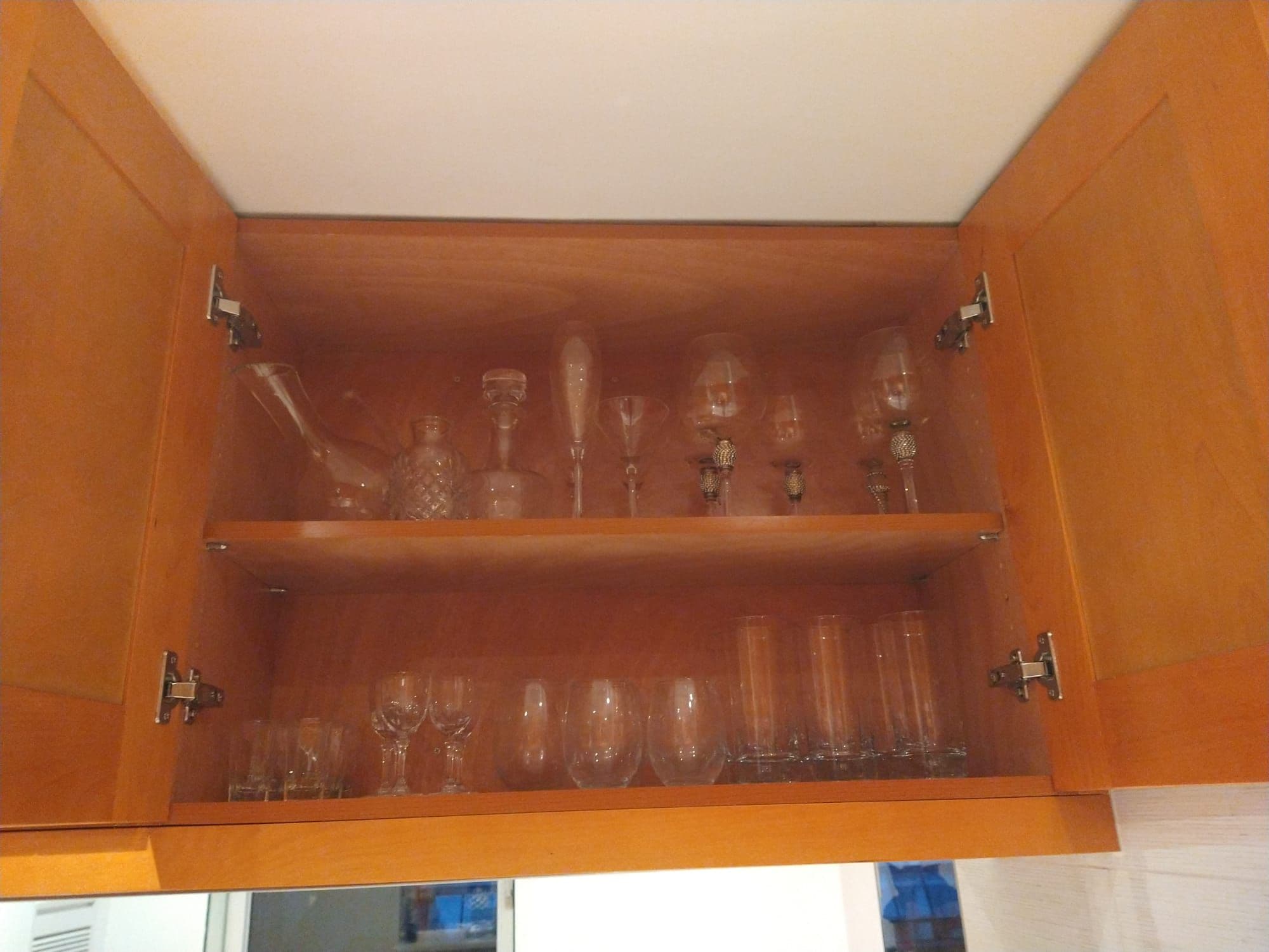 A wooden cabinet with two shelves, each holding various glassware including wine glasses and tumblers.