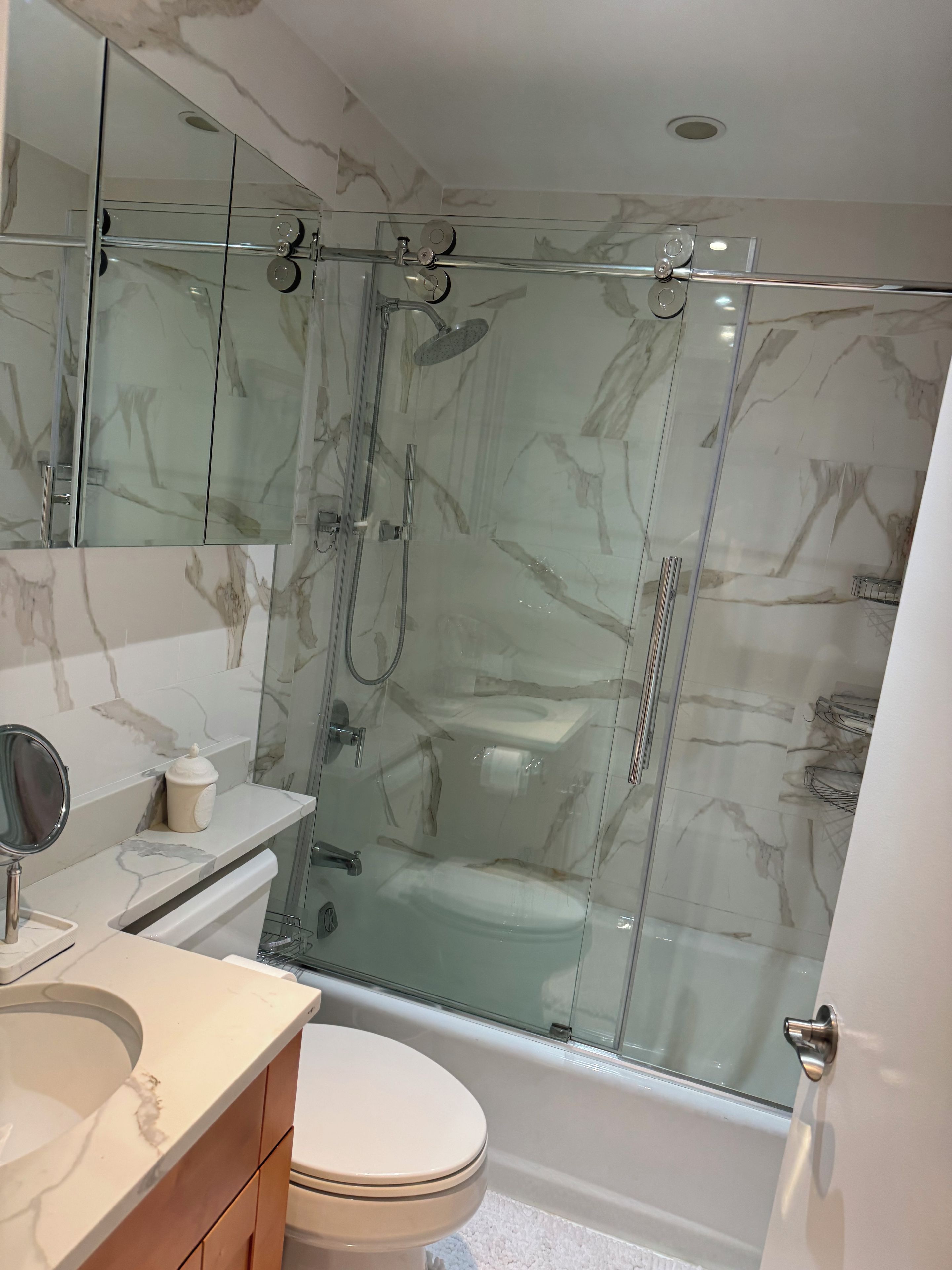 A modern bathroom with a glass-enclosed shower, a toilet, and a vanity with a mirror.