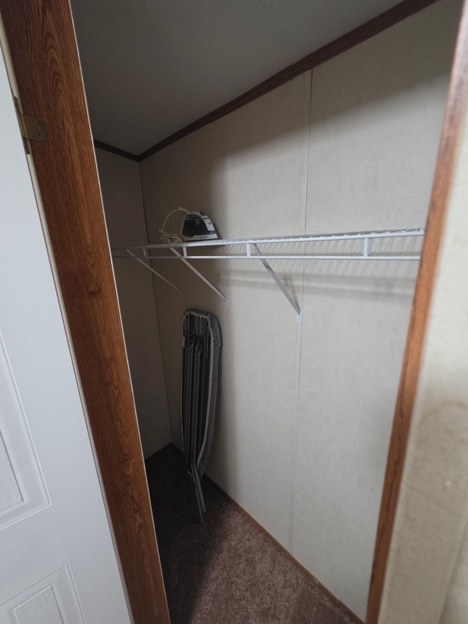 A narrow hallway with a white door on the left, a metal shelf unit against the wall, and a grey curtain hanging on the right.