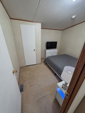 A bedroom with a bed, a dresser, a television, and a lamp.