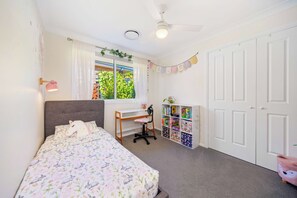 Ein Schlafzimmer mit Bett, Schreibtisch, Stuhl, Kleiderschrank und einem Fenster mit Vorhängen.