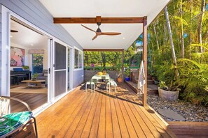 Eine Terrass mit Deckenventilator, Tisch und Stühlen sowie Blick auf einen Garten mit Palmen.
