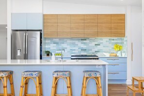 A modern kitchen with a stainless steel refrigerator, wooden cabinets, a tiled backsplash, and bar stools. - Green Oasis - Renovated family home (Port Macquarie)