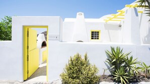 A white building with a yellow door and window, surrounded by plants. - The Architect's House (Santorini)