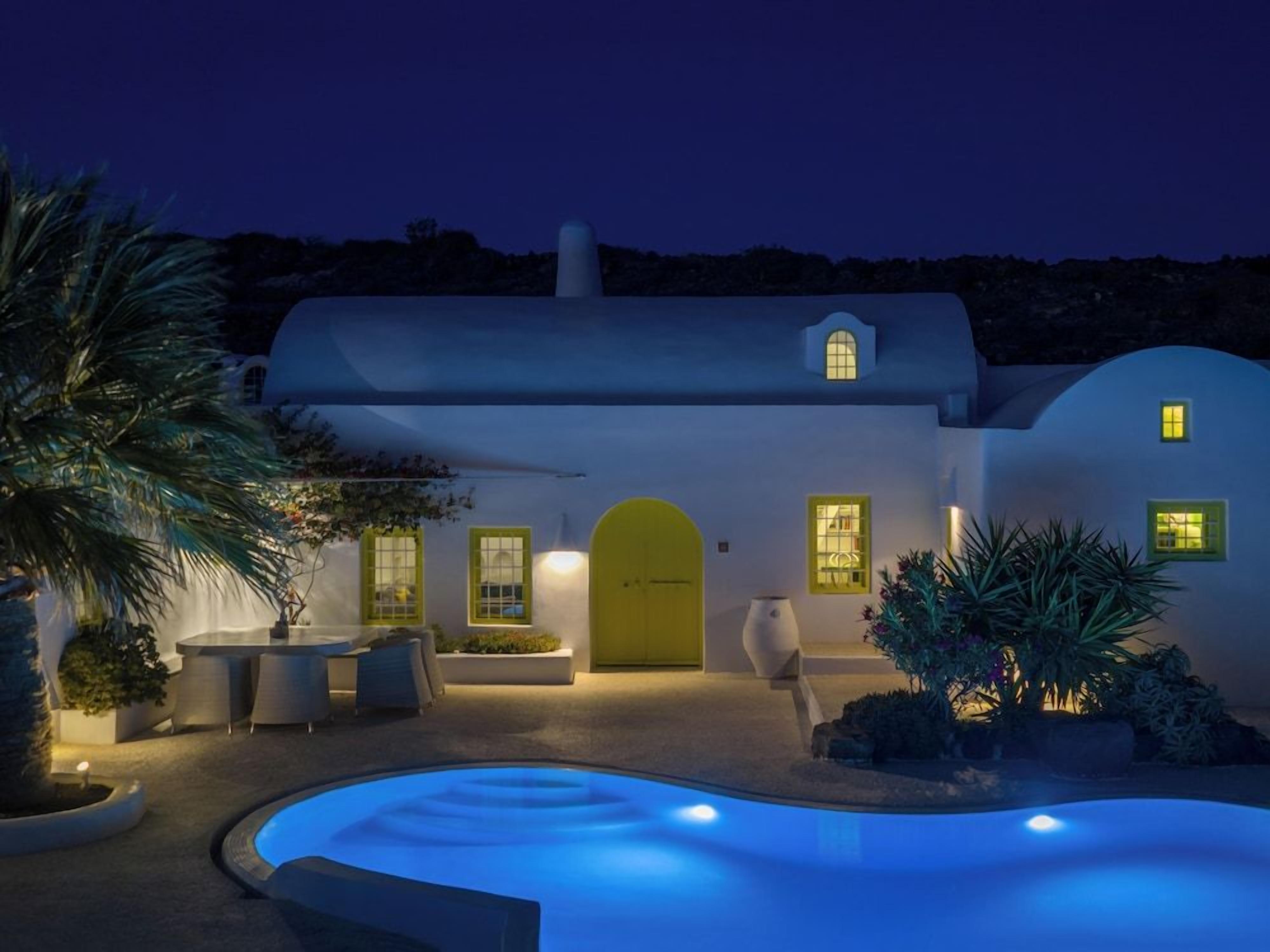 A modern villa with a swimming pool, outdoor seating, and a well-lit entrance.