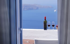 En balkon med havudsigt, en vinflaske, to vinglas og en kurve med et æble.
