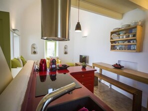 Una cocina compacta con encimera roja, extractor de acero inoxidable y estante de madera con vajilla.