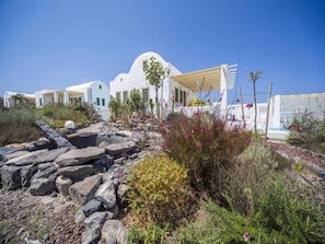 Un edificio blanco con techo curvo, rodeado de terreno rocoso y vegetación.