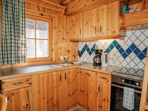 A kitchen with wooden cabinets, a window with a plaid curtain, a coffee maker, and a tiled backsplash. - Zirbenhütte by Interhome (Forstau)