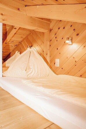 A room with a sloped ceiling, wooden walls, a bed with white bedding, and a wall-mounted light fixture.