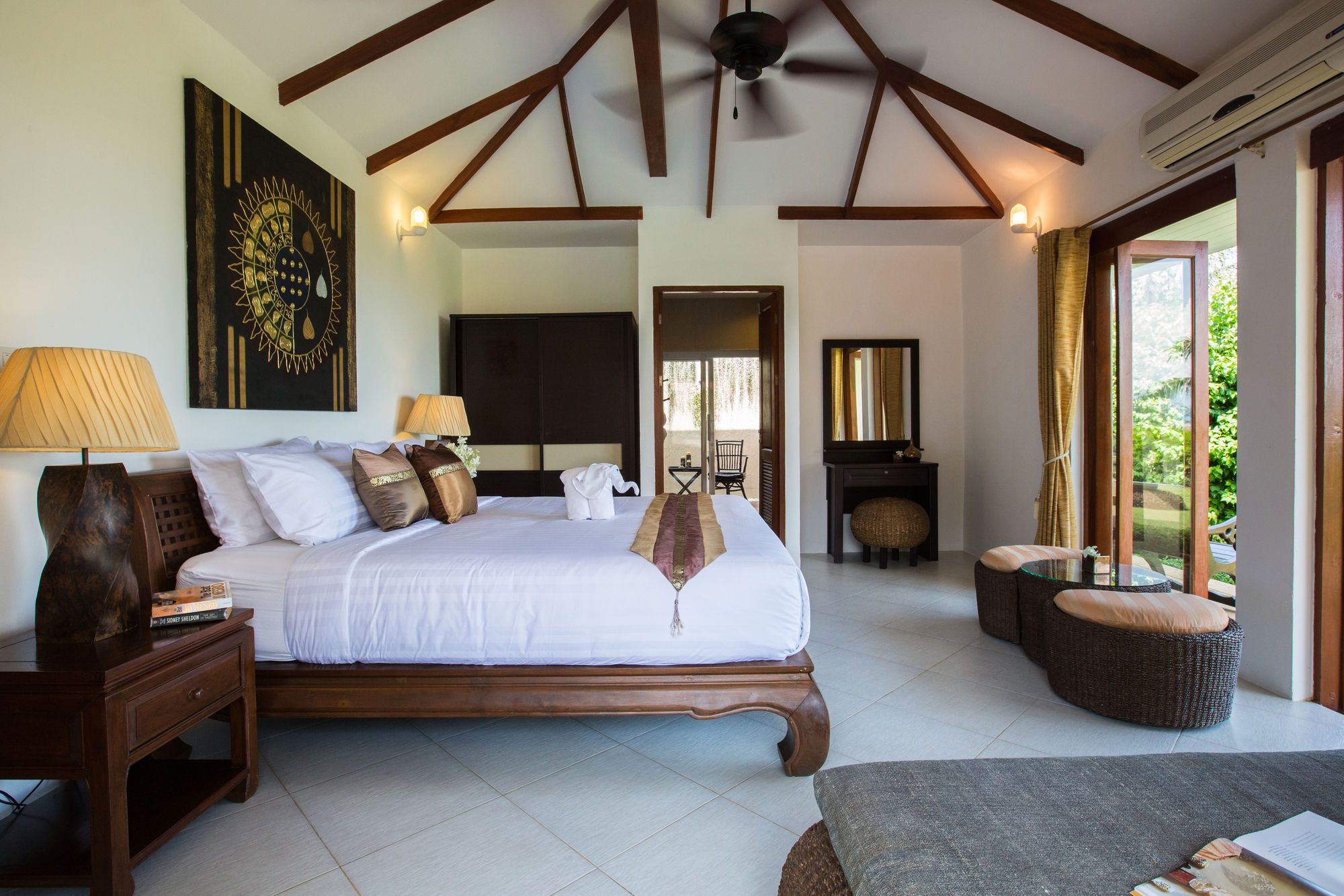 A spacious bedroom with a large bed, bedside lamps, a wooden nightstand, a wall-mounted artwork, and a view of the outdoors.