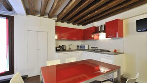 A modern kitchen with red cabinets, a glass dining table, and white chairs. - Red Rose (Venice)