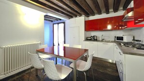 A modern kitchen with white cabinets, a red backsplash, and a wooden ceiling. - Red Rose (Venice)