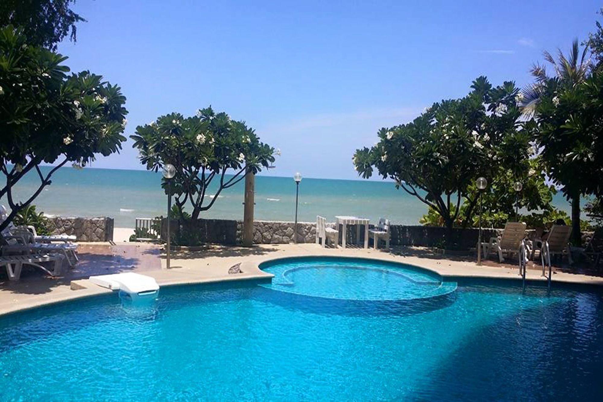 A swimming pool with a view of the ocean, surrounded by trees and lounge chairs.