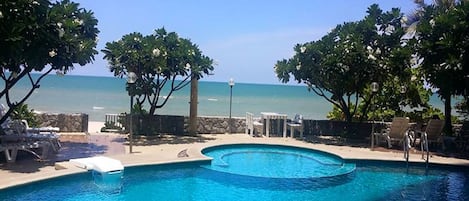 A swimming pool with a view of the ocean, surrounded by trees and lounge chairs.