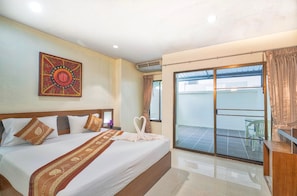 A hotel room with a bed, a decorative wall hanging, a sliding glass door to a balcony, and a small table with a chair. - Lucky Patong Hotel (Patong)