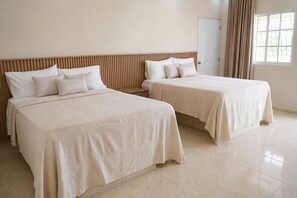 Ein Hotelzimmer mit zwei Betten, einem hölzernen Kopfteil, einer Tür und einem Fenster mit Vorhängen.