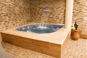 A hot tub with a blue mosaic edge, surrounded by a wooden and stone tiled floor, and a cactus in a terracotta pot. - Vrbo Property (Santo Domingo Este)
