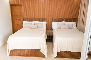 A hotel room with two beds, wooden paneling on the walls, and a small wooden bench. - Vrbo Property (Santo Domingo Este)