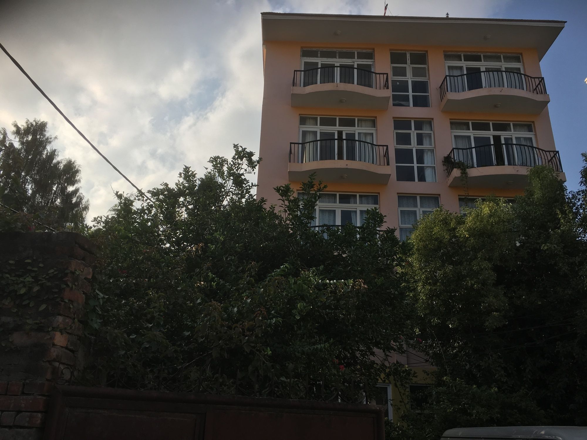A multi-story building with balconies, surrounded by dense foliage.