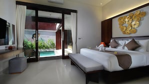 A modern hotel room with a large bed, a bench, a TV, a desk, and a view of a pool and greenery.
