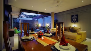 A dining area with a table set for two, a sofa, and a Buddha statue on the wall.