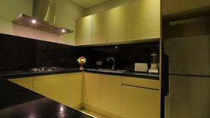 A modern kitchen with wooden cabinets, a black countertop, a stainless steel range hood, a sink, and a refrigerator.