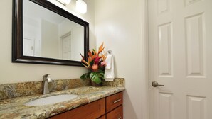 A bathroom with a granite countertop, a sink, a mirror, a towel, and a door. - Oceanfront - Luxury View - 2 Beds (Lahaina)