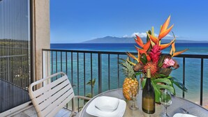 A table with a bottle of wine, a glass, and a pineapple on a balcony with a view of the ocean and a mountain. - Oceanfront - Luxury View - 2 Beds (Lahaina)